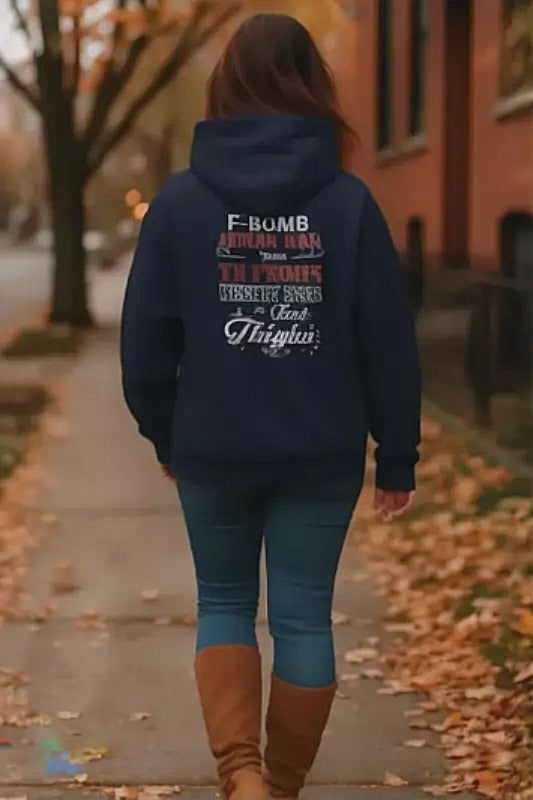 A person wearing a navy blue hoodie with text printed on the back is walking down a sidewalk lined with fallen leaves.