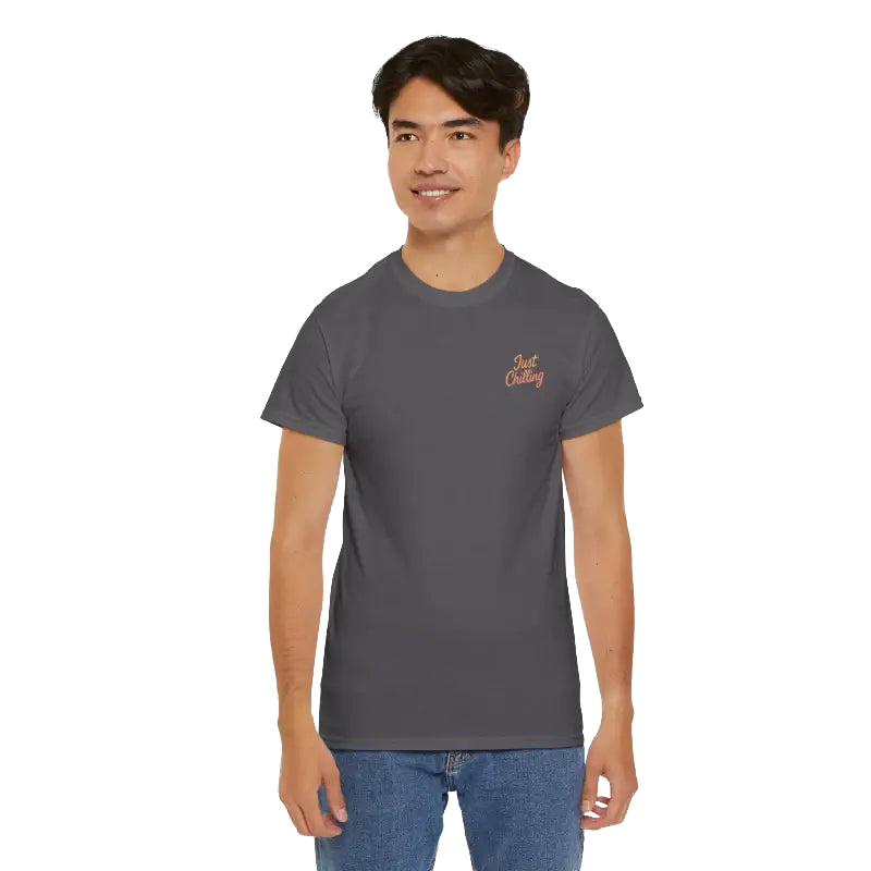 A young man wearing a gray t-shirt with a logo on the left side of his chest, standing against a black background.