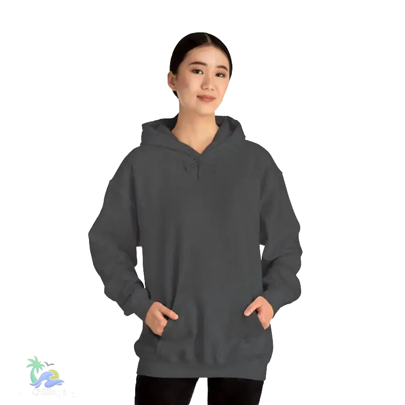 A woman wearing a gray hoodie stands against a black background, looking directly at the camera with a neutral expression.