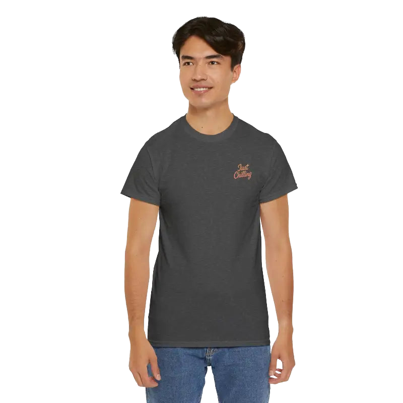 A young man wearing a gray t-shirt with a logo on the left side of his chest, standing against a black background.