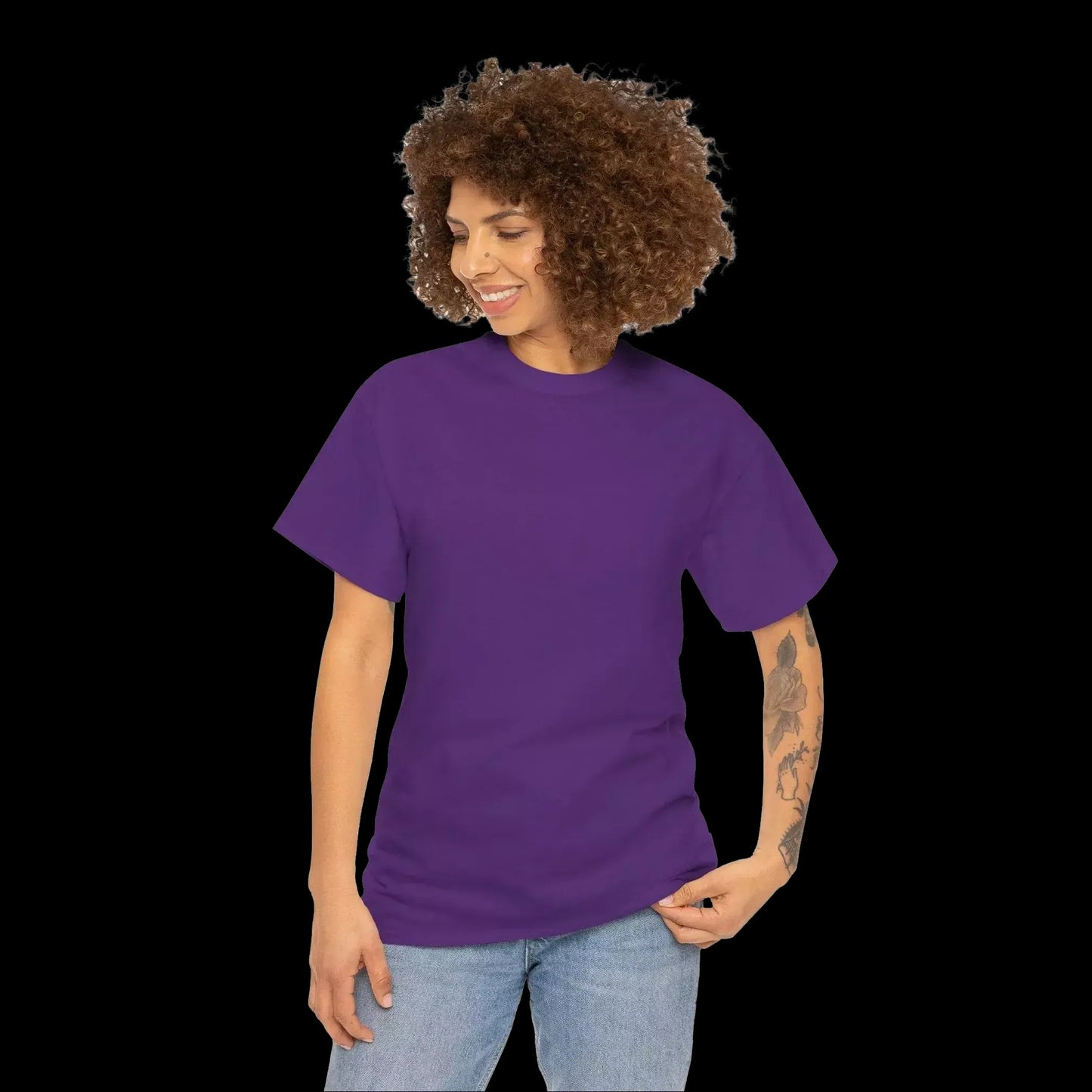 A woman with curly hair wearing a purple t-shirt and jeans is smiling and looking down at her hand.