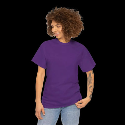 A woman with curly hair wearing a purple t-shirt and jeans is smiling and looking down at her hand.