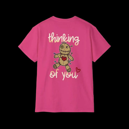 A pink t-shirt with a cartoon voodoo doll and the text "Thinking of you" printed on it.