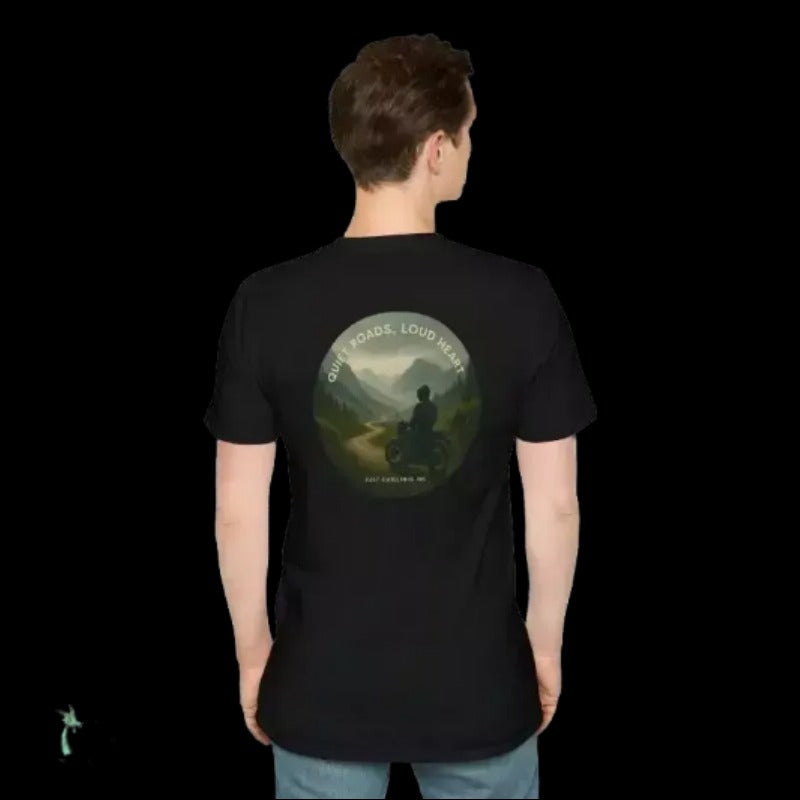 A person wearing a black t-shirt with a graphic design on the back, depicting a person riding a motorcycle on a road surrounded by mountains.