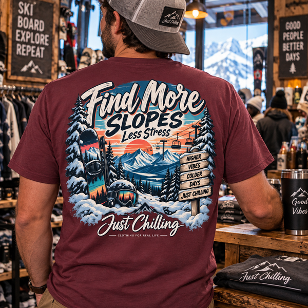 Maroon tee back graphic with snowy mountains, pine trees, ski lift, and 'Find More Slopes Less Stress' text in a rustic shop
