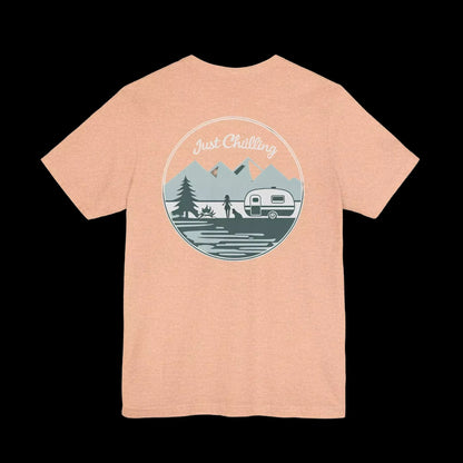 A peach-colored t-shirt with a graphic design featuring a camping scene with a camper van, mountains, and a person in the background.