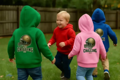 A group of young children wearing colorful hoodies with football helmets on them, standing on a grassy field.