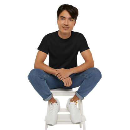 A young man wearing a black t-shirt and blue jeans is sitting on a white stool, with his hands crossed and a smile on his face.