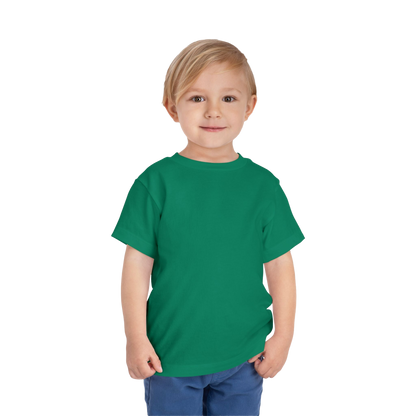 A young boy with blonde hair is wearing a green t-shirt and blue pants, smiling at the camera.