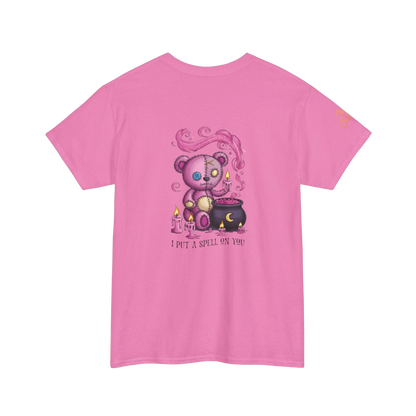 A pink t-shirt with a graphic design depicting a purple teddy bear holding a cauldron and surrounded by flames, with the text "I put a spell on you" below the image.
