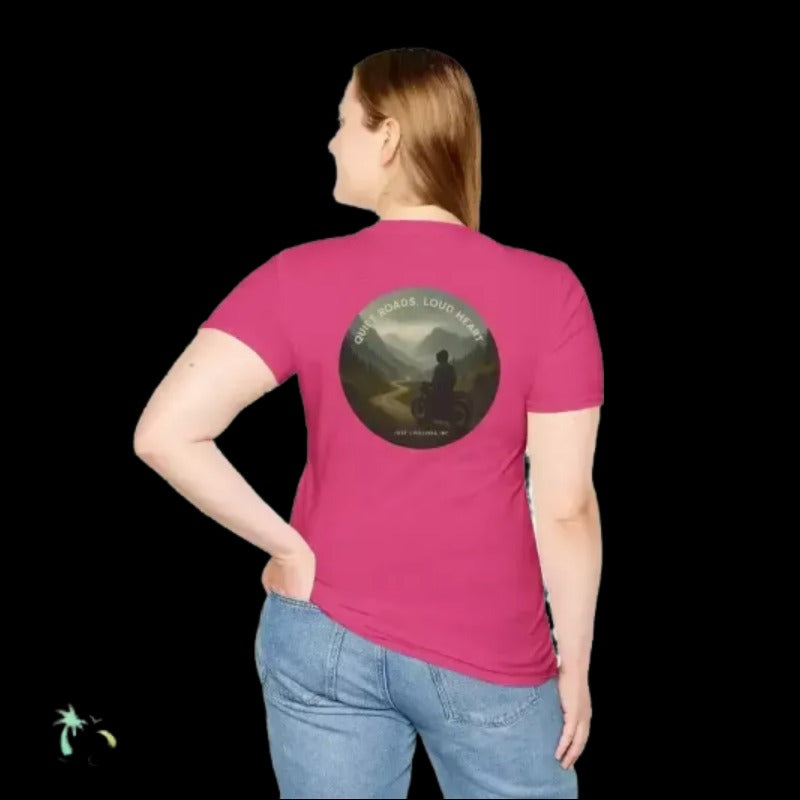A woman wearing a pink t-shirt with a graphic design on the back is standing against a black background.