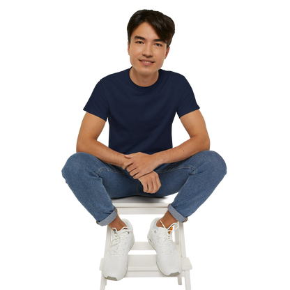 A young man wearing a navy blue t-shirt and blue jeans is sitting on a white stool, with his hands crossed and a smile on his face.
