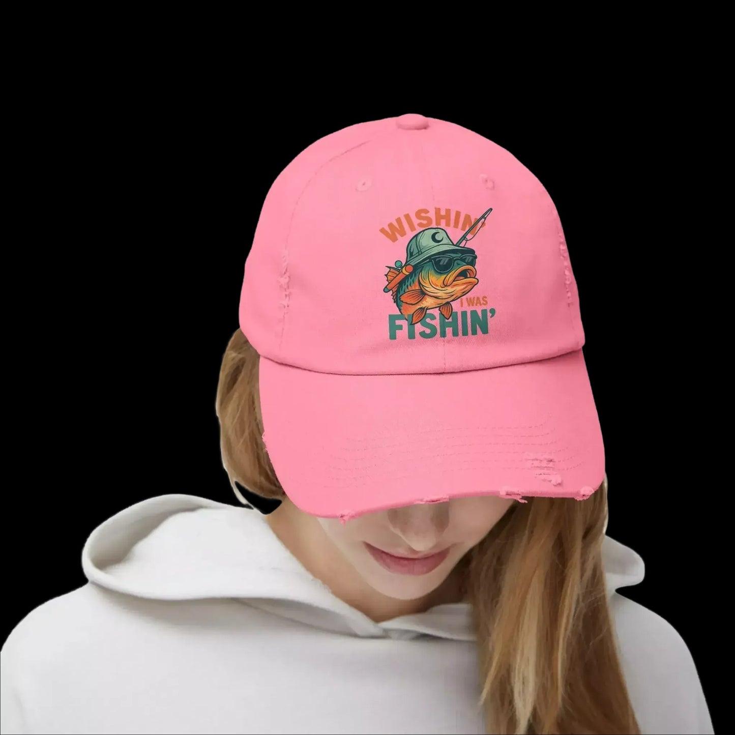 A person wearing a pink baseball cap with a fish graphic and the text "WISHIN' THE FISHIN'" printed on it.