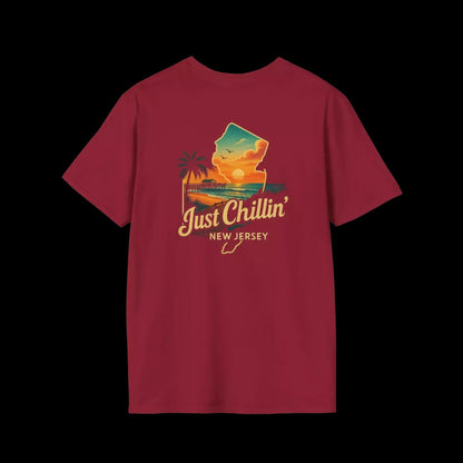 A red t-shirt with a graphic design depicting a sunset over a beach and palm trees, along with the text "Just Chillin' NEW JERSEY".