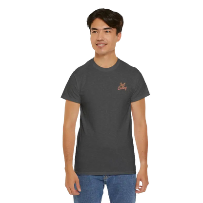 A young man wearing a gray t-shirt with a logo on the left side of his chest, standing against a black background.
