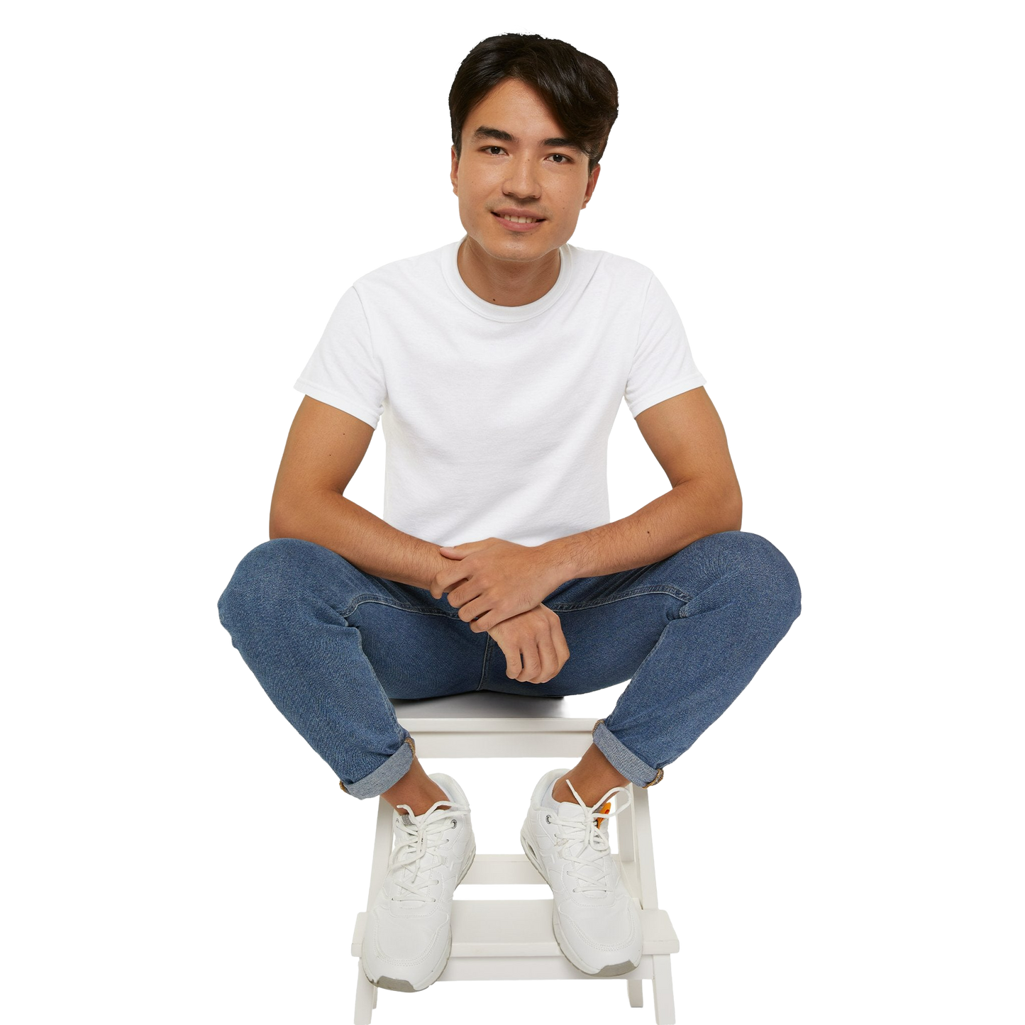 A young man wearing a white t-shirt and jeans is sitting on a white stool, smiling at the camera.