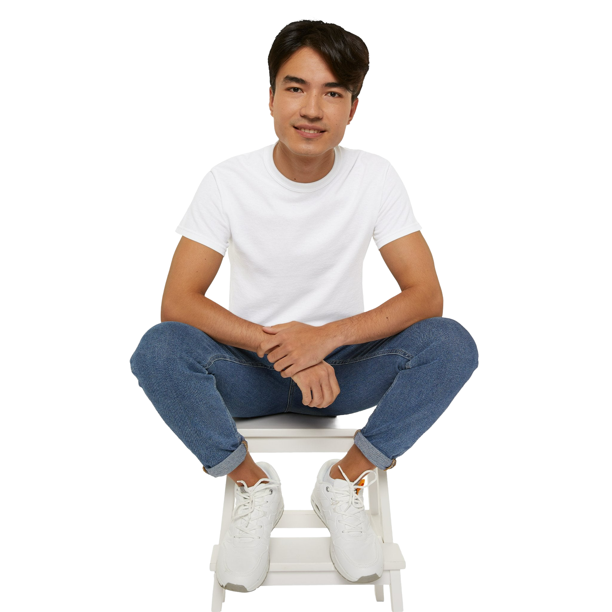 A young man wearing a white t-shirt and jeans is sitting on a white stool, smiling at the camera.