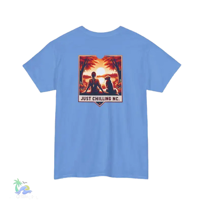 A blue t-shirt with a graphic design depicting two people sitting in a tropical setting, with a sunset in the background. The text below the graphic says "JUST CHILLING MC".