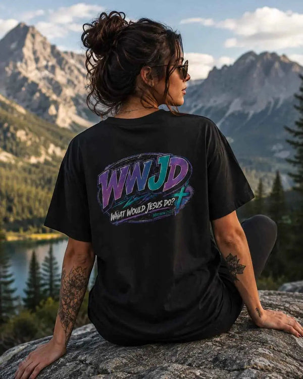 Just Chilling Shop black cotton graphic tee with retro 90s WWJD back print, worn by a woman outdoors near mountains.