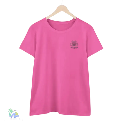A pink t-shirt with a graphic design on the front, hanging on a wooden hanger against a black background.